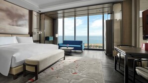 Habitación de hotel moderna con una cama grande, zona de estar con vistas al mar y una mesa de comedor.