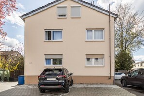 Un bâtiment beige de deux étages, doté de quatre fenêtres, avec un VUS garé devant et un baril bleu.