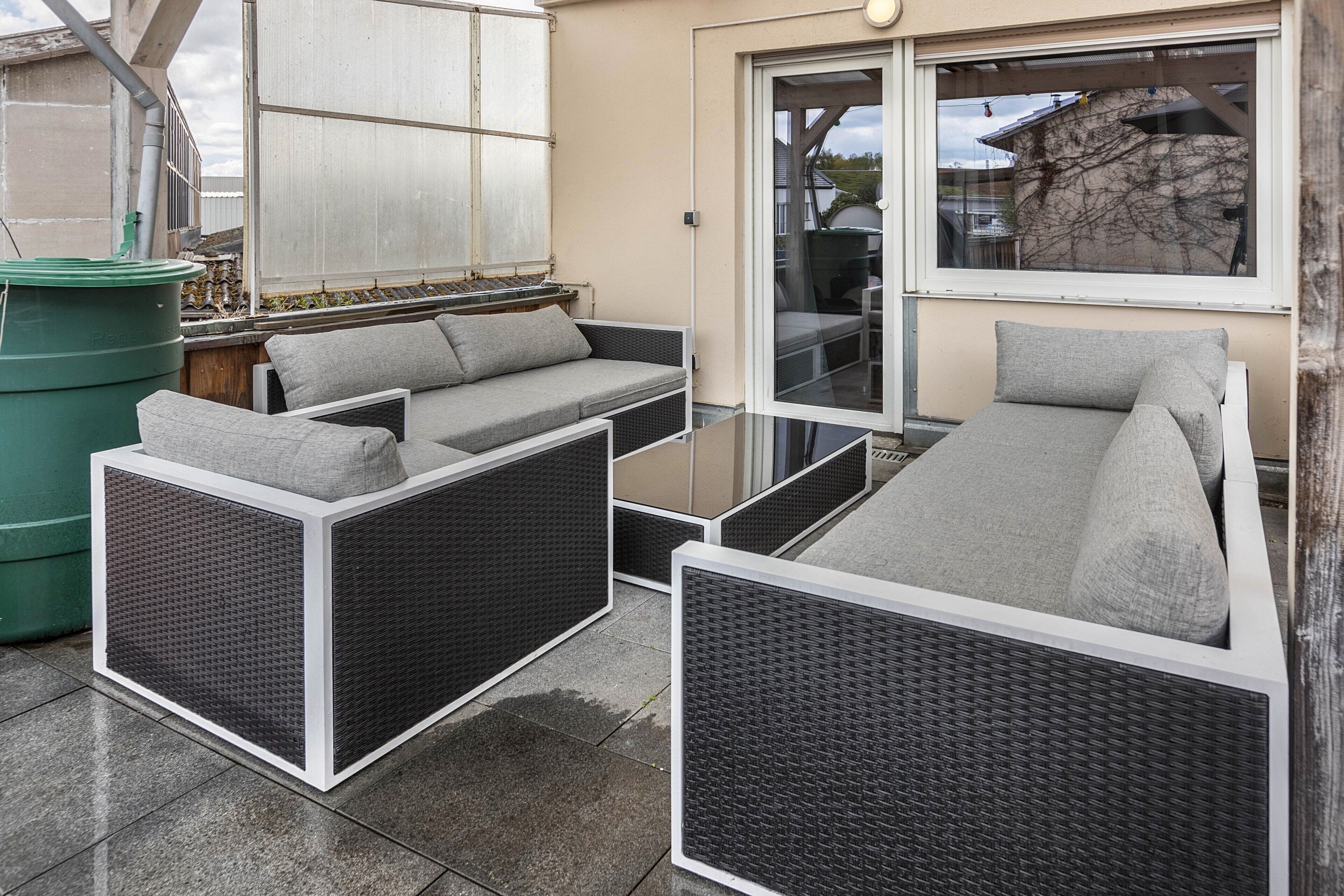 Eine Terrasse mit Korbmöbeln, einem grünen Fass und einer Schiebetür.
