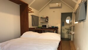A small, cozy bedroom with a single bed, a wooden nightstand, a desk with a microwave, a small sink, and a mirror. - Walden Koh Lanta Tiny Homes by the Sea (Ko Lanta)