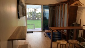 A compact kitchen with a wooden table, stools, and a view of a grassy area through a glass door. - Walden Koh Lanta Tiny Homes by the Sea (Ko Lanta)