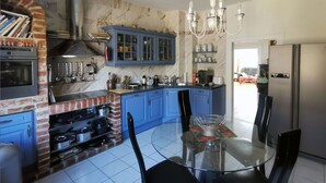 A kitchen with a brick oven, blue cabinets, a glass dining table, and a stainless steel refrigerator.