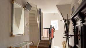 A hallway with a staircase, a mirror, a glass console table, and a coat rack.