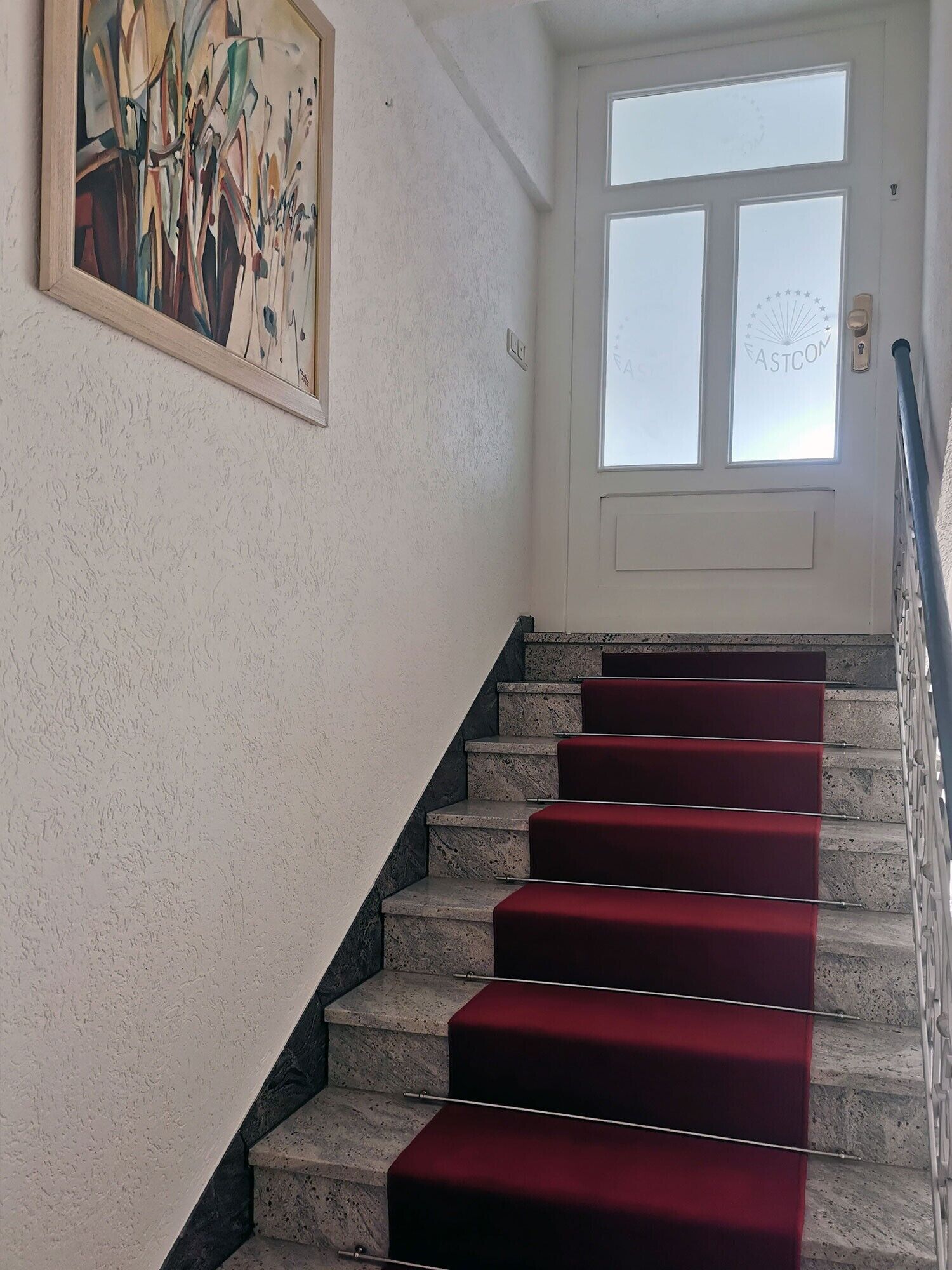 Eine Treppe mit roten Teppichstufen, ein Bild an der Wand und eine Tür mit satinierten Glasscheiben.