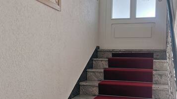 Eine Treppe mit roten Teppichstufen, ein Bild an der Wand und eine Tür mit satinierten Glasscheiben.