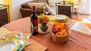 A dining table set with plates, cutlery, a wine bottle, a vase with flowers, and a basket of fruit.