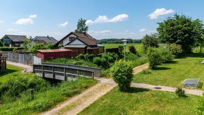 A rural setting with a wooden bridge, a red barn, and houses with sloped roofs.