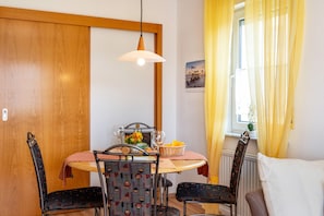 Un espace repas comprenant une table, des chaises, un luminaire suspendu et une fenêtre avec des rideaux.