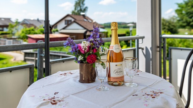 A table with a bottle and glasses on a balcony with a view of houses.