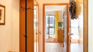 A hallway with a wooden door, a coat rack, and a glimpse of a room with a yellow curtain.