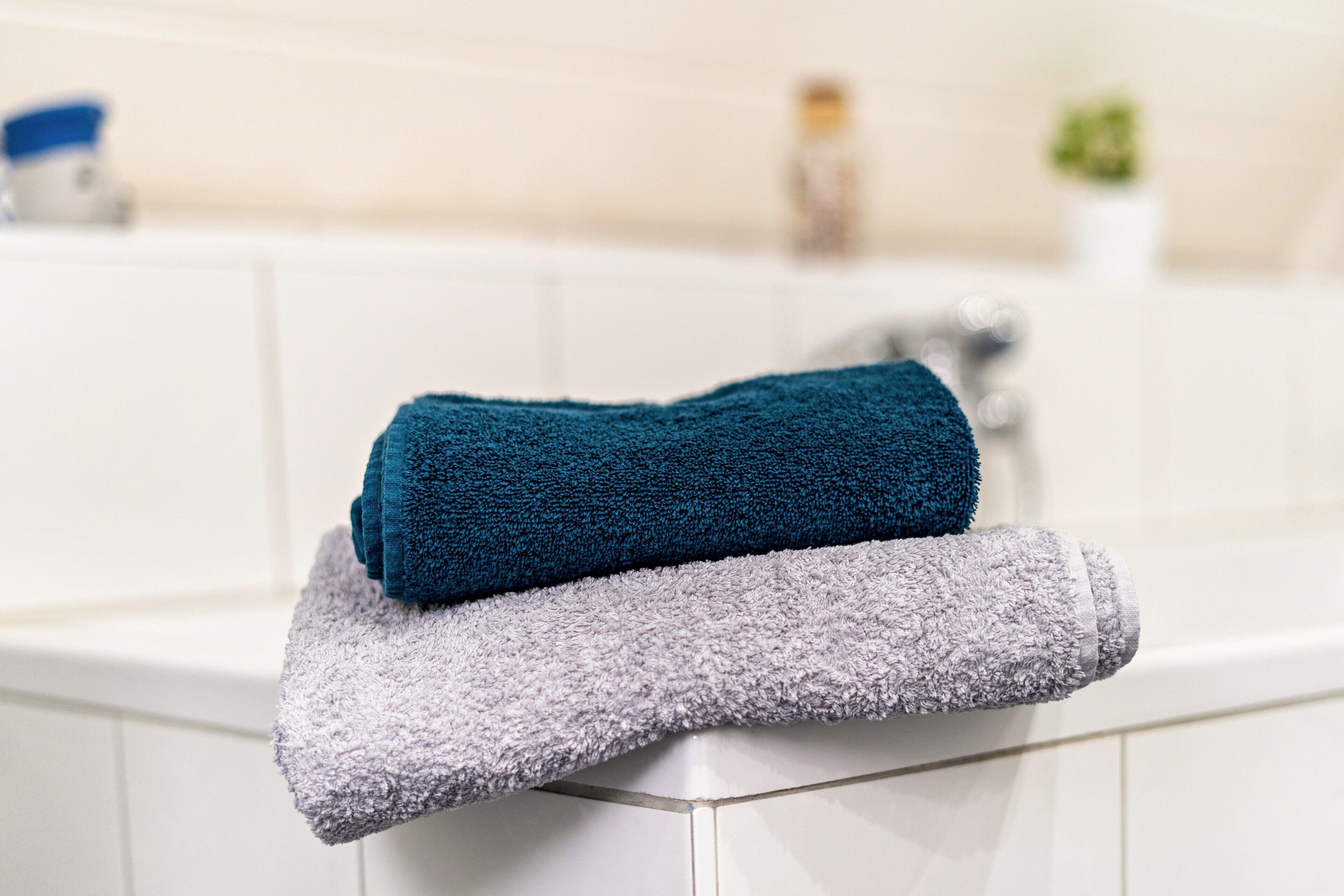 Un baño con pared de azulejos blancos, un grifo plateado y dos toallas apiladas sobre una bañera blanca.
