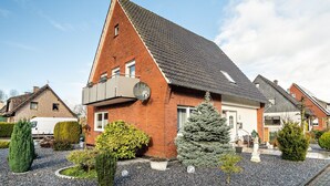 Un immeuble résidentiel doté d’un toit en pente, d’un garage et d’un jardin bien entretenu, agrémenté de divers arbustes et d’un sapin de Noël.