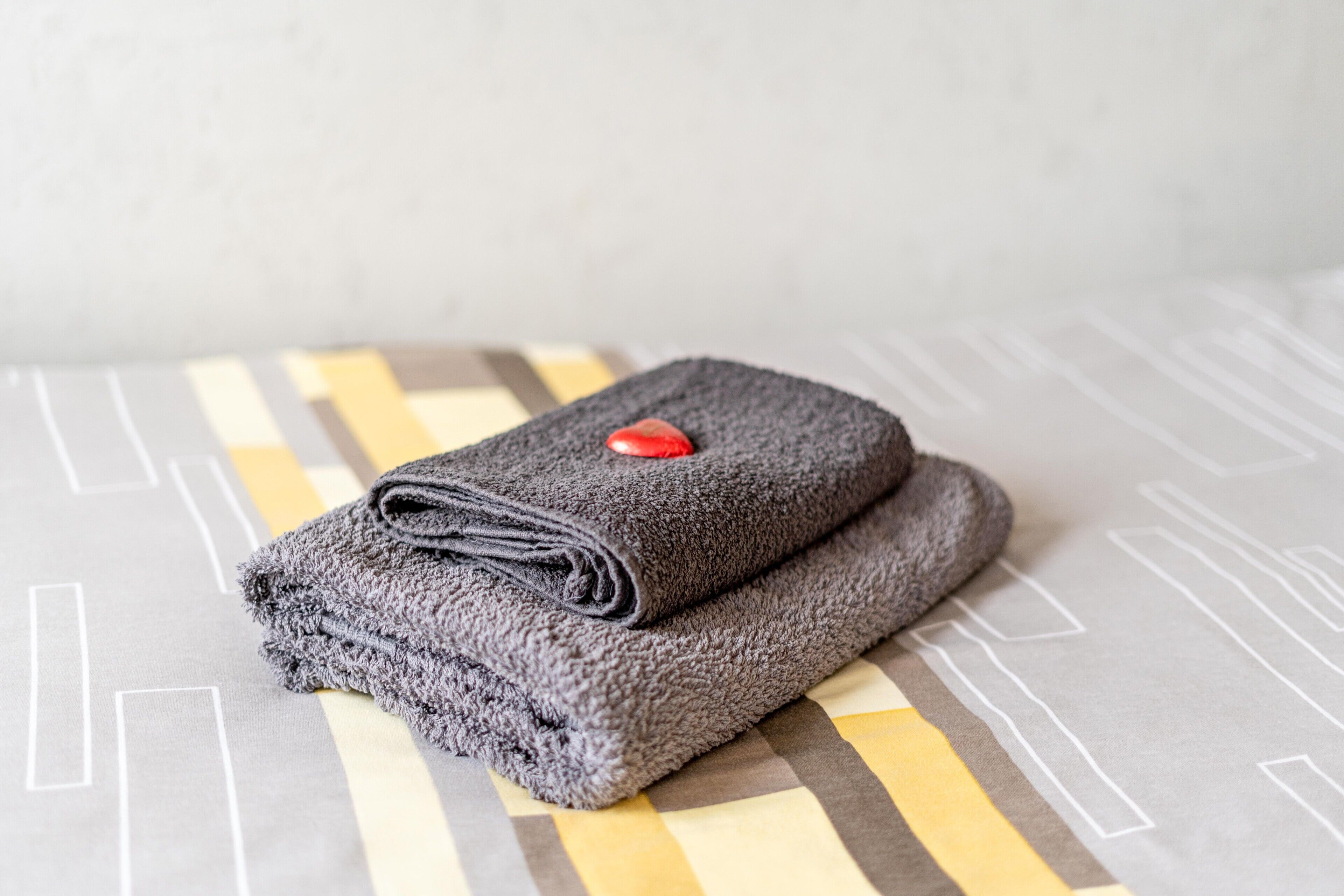 A neatly folded gray towel with a red button on a bed with a geometric patterned bedspread.