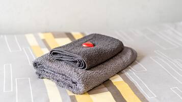 A neatly folded gray towel with a red button on a bed with a geometric patterned bedspread.