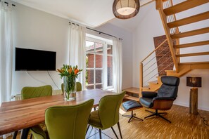 Un soggiorno moderno con un tavolo da pranzo in legno, sedie verdi, un divano in pelle nera, una TV montata a parete e una scala con ringhiera in legno.