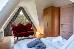 Una camera da letto con soffitto spiovente, una sedia rossa, un armadio in legno e un letto con lenzuola bianche.