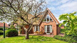 A brick house with a triangular roof, a tree in the yard, and a patio with chairs. - Holiday Home 'Altes Fischerhaus Döse' with Private Garden and Wi-Fi (Cuxhaven)