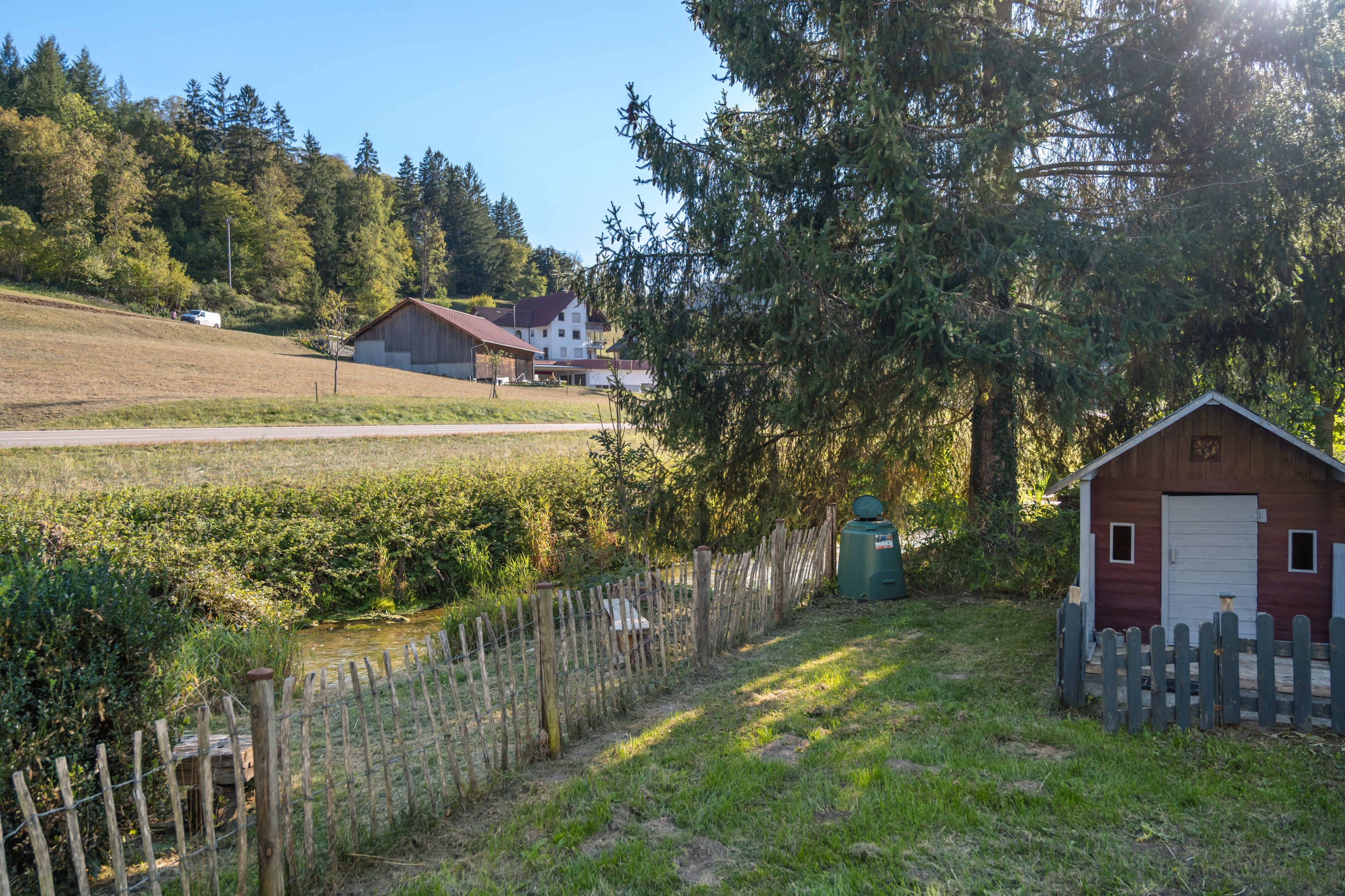 A rural landscape with a small wooden shed, a fenced area, and a road in the distance.