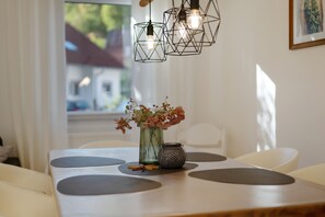 A dining table with a vase of flowers and a candle, set against a window with a view of buildings. - Bibernest Holiday Home with Private Terrace, AlbCard Partner (Münsingen)