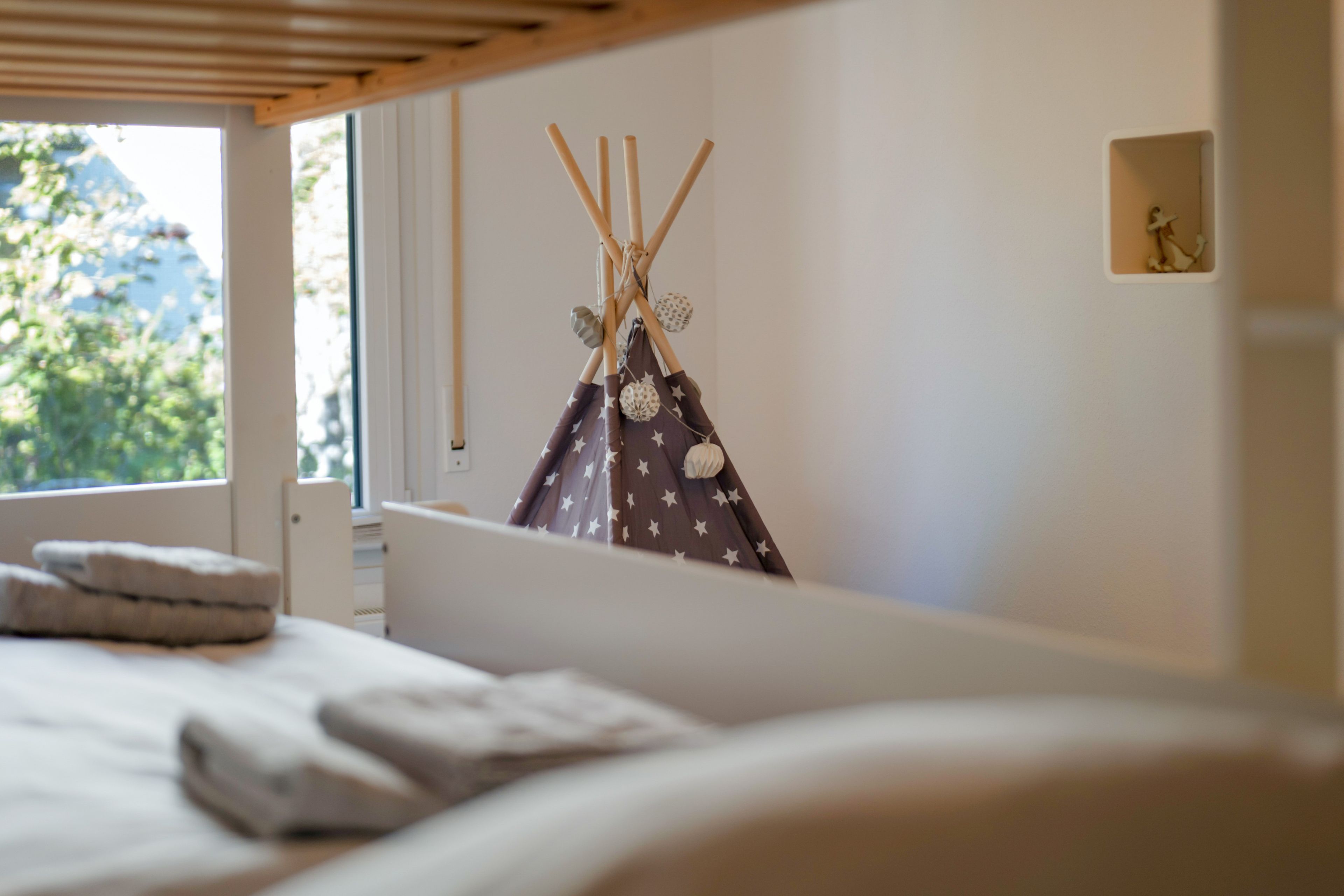 A bed with pillows, a window with blinds, and a wall with a star-patterned item.