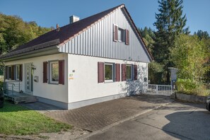 Ein zweistöckiges Gebäude mit Satteldach, einer Veranda und einem kleinen Garten.