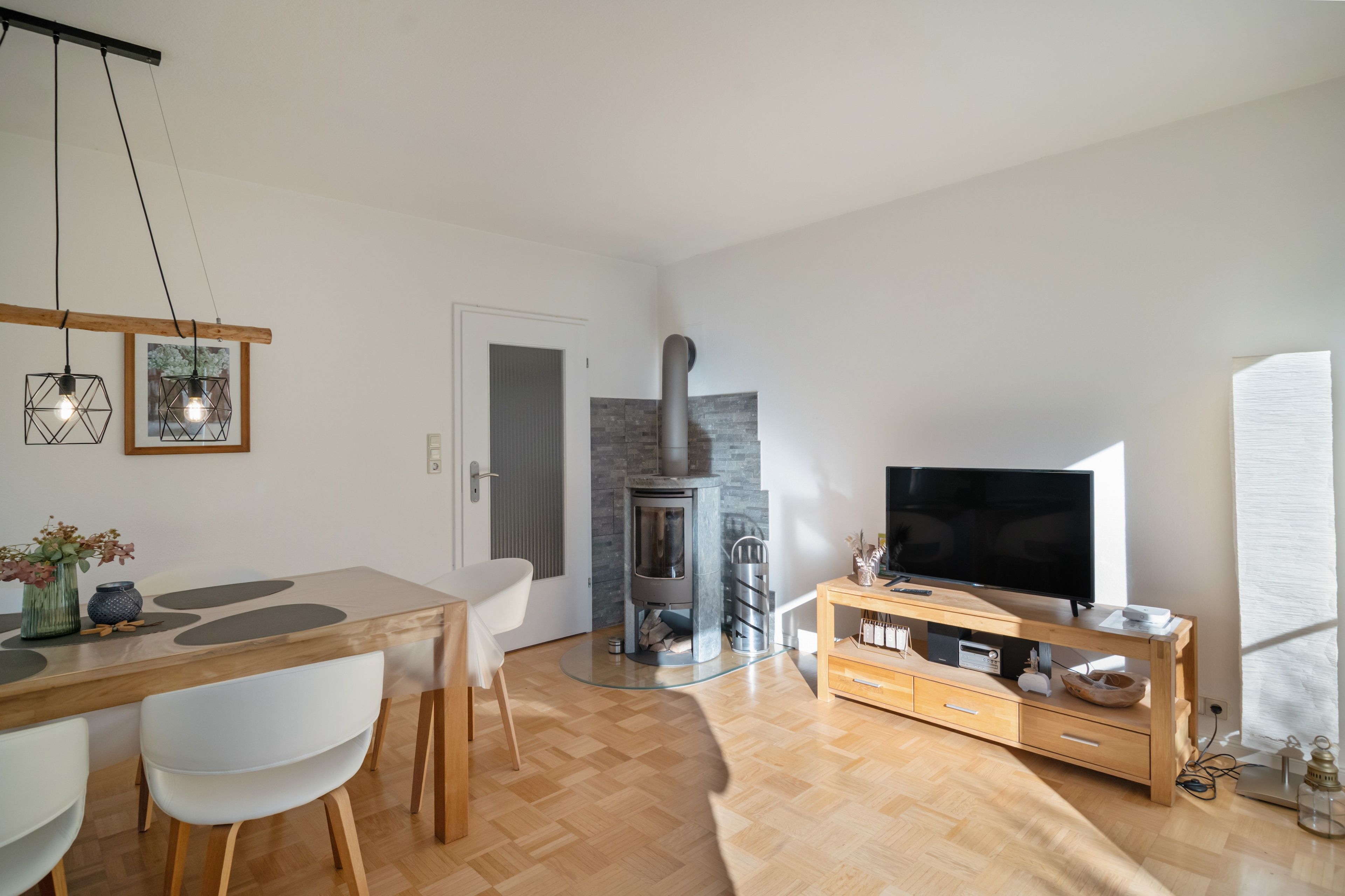 Ein modernes Wohnzimmer mit einem Holzespeisetisch, weißen Stühlen, einem Fernseher und einem Kamin.