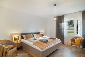 A modern bedroom with a large bed, bedside lamps, a wicker chair, and a view of the outdoors. - Bibernest Holiday Home with Private Terrace, AlbCard Partner (Münsingen)
