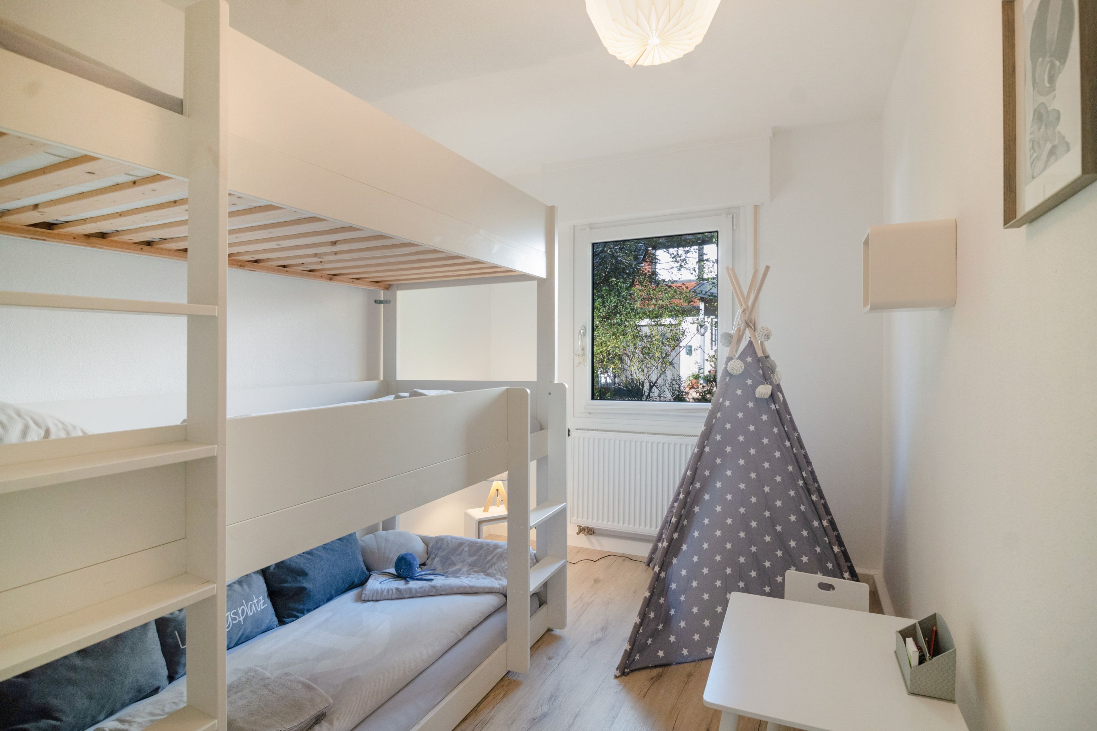 A child's bedroom with bunk beds, a sofa, a desk, and a window with a view of the outside.