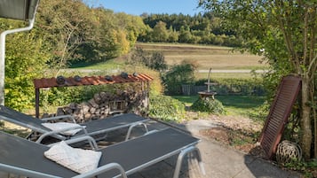 Un patio con mesa y sillas, un muro de piedra y vistas a un paisaje rural.