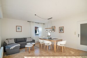 A modern living room with a grey sofa, a dining table with chairs, a hanging light fixture, and a door. - Bibernest Holiday Home with Private Terrace, AlbCard Partner (Münsingen)