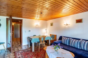 Um quarto com teto de madeira, uma mesa de jantar com toalha xadrez, um sofá com almofadas listradas e um tapete vermelho estampado.