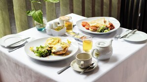 Une table dressée avec des plats pour le petit-déjeuner, notamment des œufs Bénédicte et des toasts, une théière et une petite plante.
