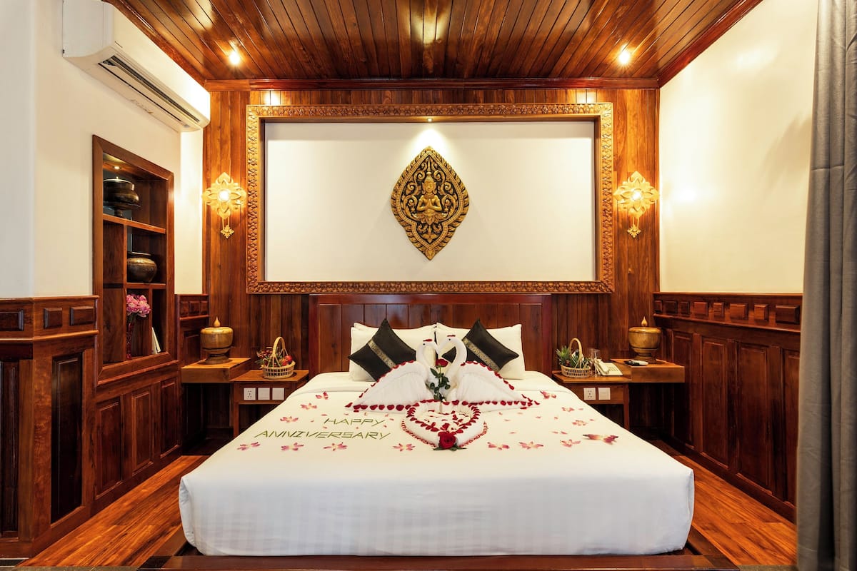 Une chambre élégamment aménagée, dotée d’un grand lit, de coussins décoratifs, d’un miroir fixé au mur et d’un plafond en bois.