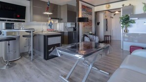 Eine moderne Küche mit Kochinsel, Essbereich mit Glastisch und Wohnbereich mit Sofa und Fernseher.