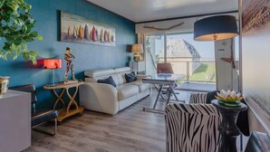Ein modernes Wohnzimmer mit blauer Akzentwand, einem weißen Sofa, einem Glastisch und einem Sessel mit ZEBRA-Muster.