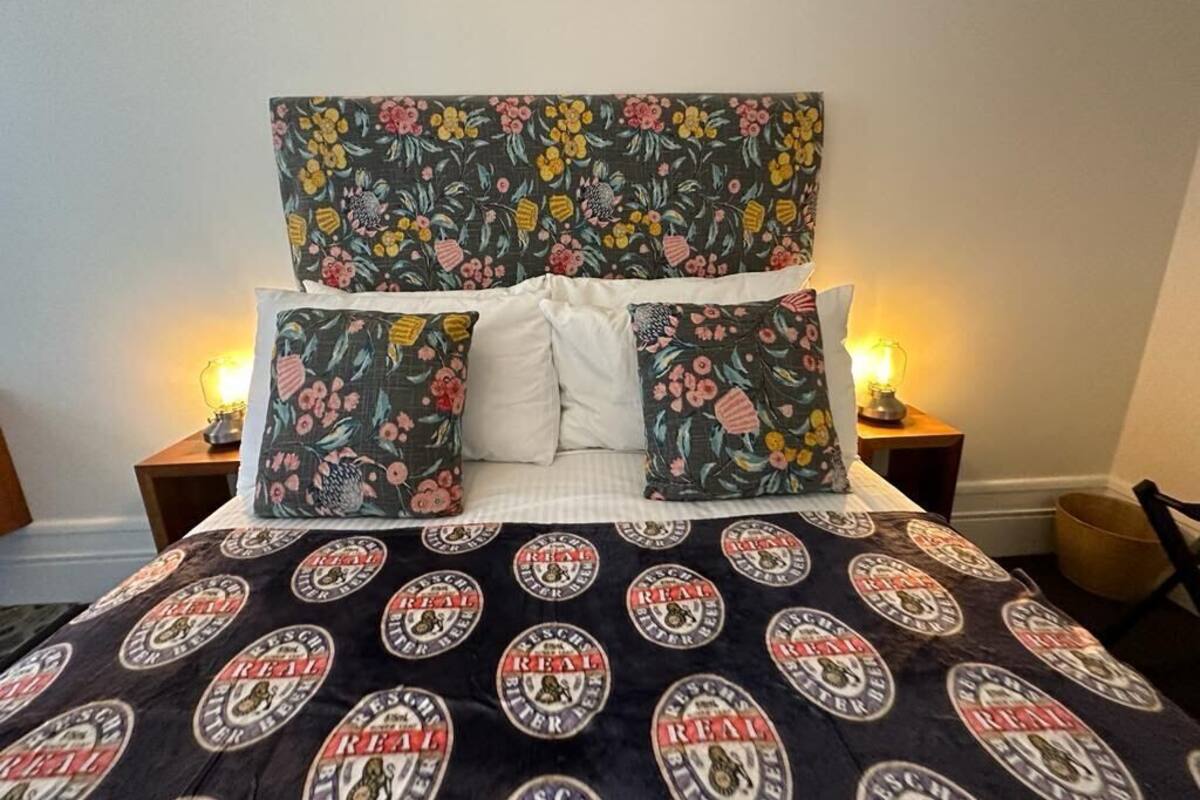 Una cama con cabecera de estampado floral, almohadas blancas y una manta oscura con diseños circulares.