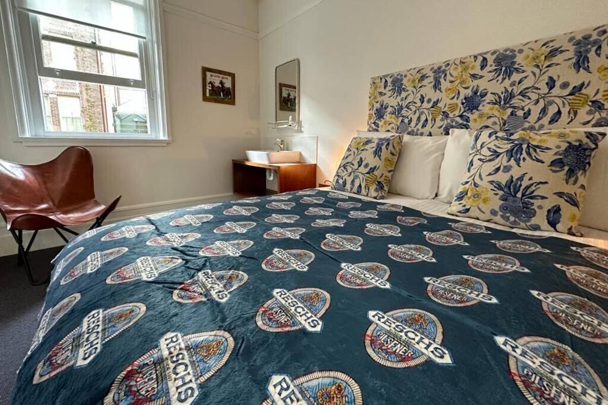 Un dormitorio con cabecera de flores, cama con cubrecama estampado, mesita de noche y una silla.