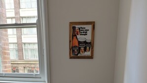 Une pièce d’angle avec un fauteuil en cuir marron, une fenêtre et une affiche encadrée au mur.