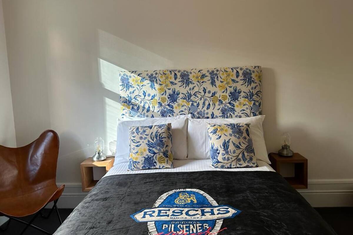 Un dormitorio con una cama con cabecera de flores blanco y negro, una butaca de cuero marrón y una mesita de noche con lámpara.
