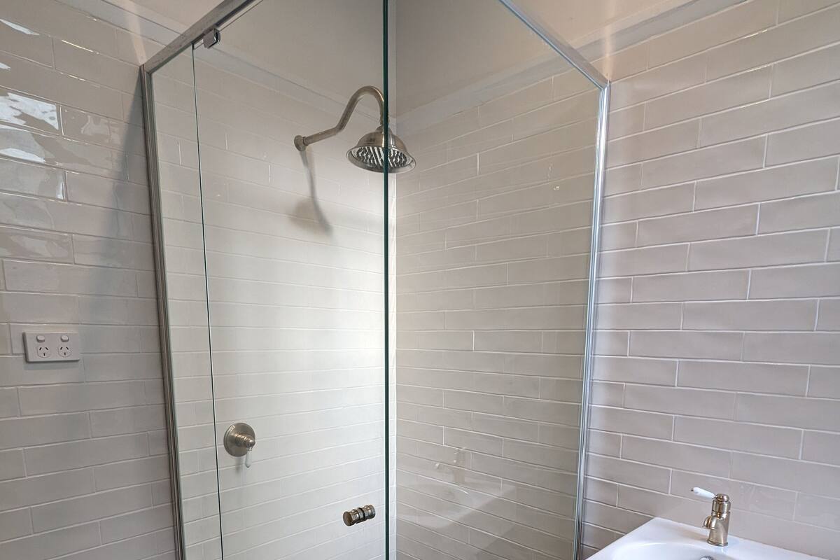 Un baño moderno con ducha envuelta en vidrio, lavamanos blanco y baldosas de suelo con diseño.