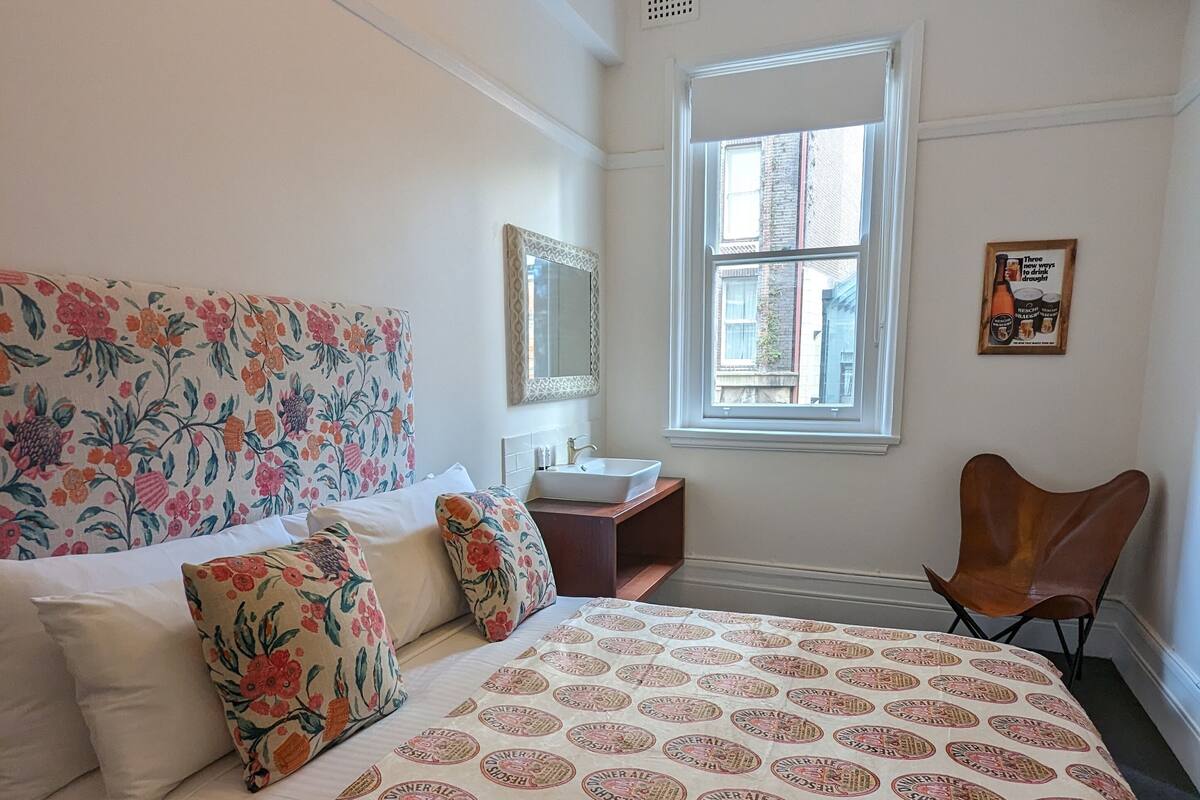 Un dormitorio con una cama grande, una mesita de noche, una ventana y una silla.