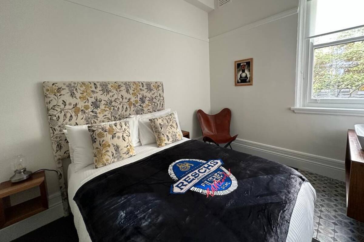 Un dormitorio con una cama, una silla, un ventanal y un cuadro en la pared.