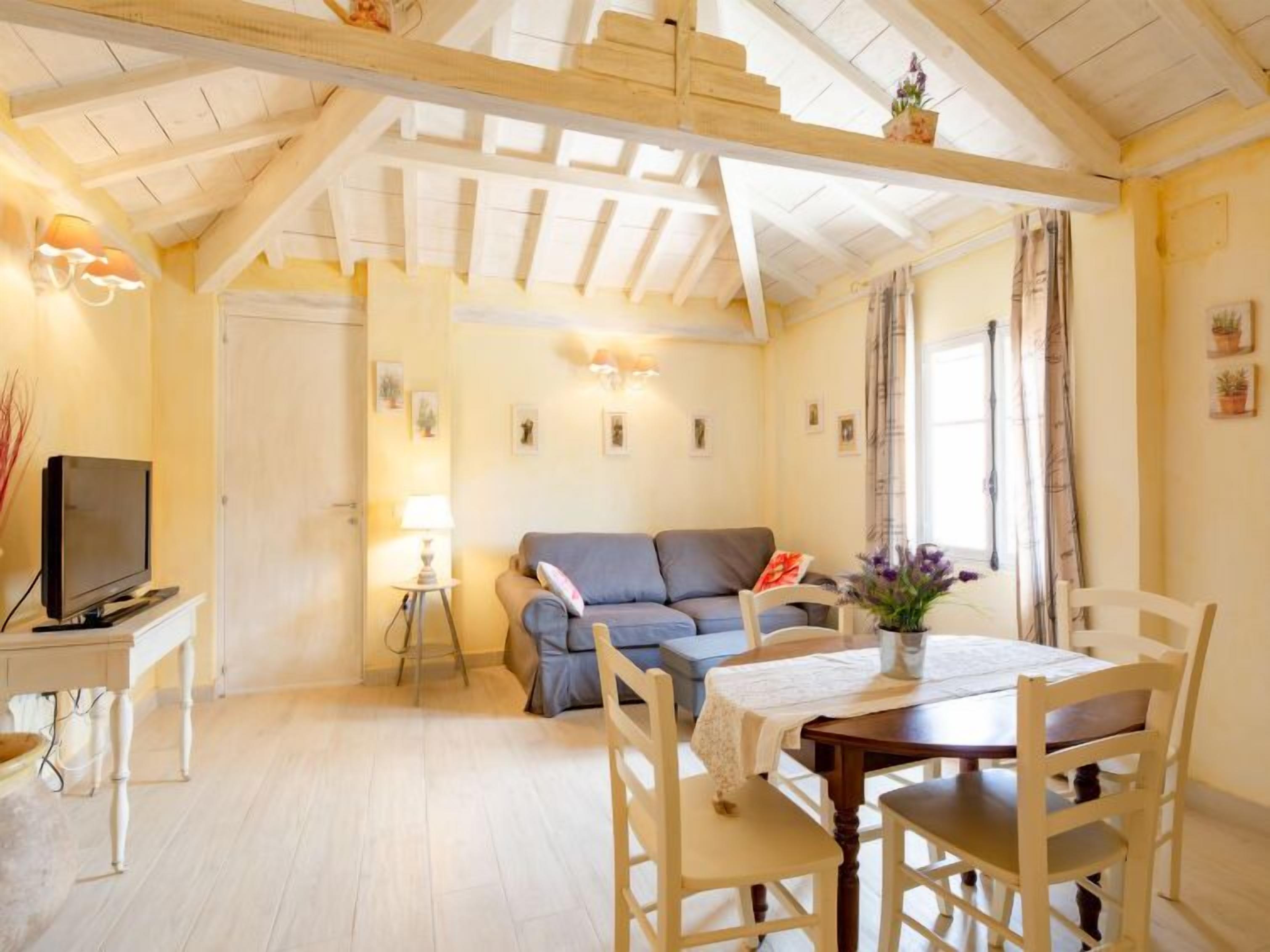 Een gezellige woonkamer met een houten plafond, een bank, een televisie en een eettafel met stoelen.