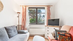 Una sala de estar con un sofá gris, un sofá rojo, una mesa de centro blanca y un televisor sobre un mueble de madera.