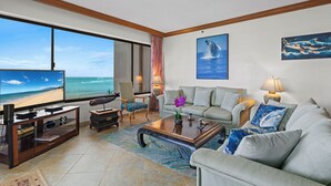 A living room with a large TV, comfortable seating, a coffee table, and a view of the ocean. - MILLION DOLLAR VIEW!!  2 BDRM OCEANFRONT CONDO WEST MAUI. NEW AC IN EVERY ROOM. (Lahaina)