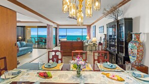 A dining area with a view of the ocean, a chandelier, and a traditional cabinet with decorative items. - MILLION DOLLAR VIEW!!  2 BDRM OCEANFRONT CONDO WEST MAUI. NEW AC IN EVERY ROOM. (Lahaina)
