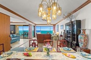 A dining area with a view of the ocean, a chandelier, and a traditional cabinet with decorative items.