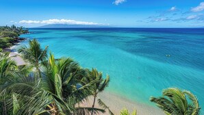 A tropical beach with clear turquoise waters, palm trees, and a distant mountain. - MILLION DOLLAR VIEW!!  2 BDRM OCEANFRONT CONDO WEST MAUI. NEW AC IN EVERY ROOM. (Lahaina)