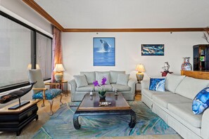 A living room with a sofa, armchairs, a coffee table, and a large window with curtains.