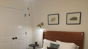 A neatly made bed with white linens and two rolled towels, a wooden headboard, a small round table with a lamp, and two framed botanical prints on the wall. - Cozy Retreat • King Bed & Kitchen Near Lee (Cleveland)